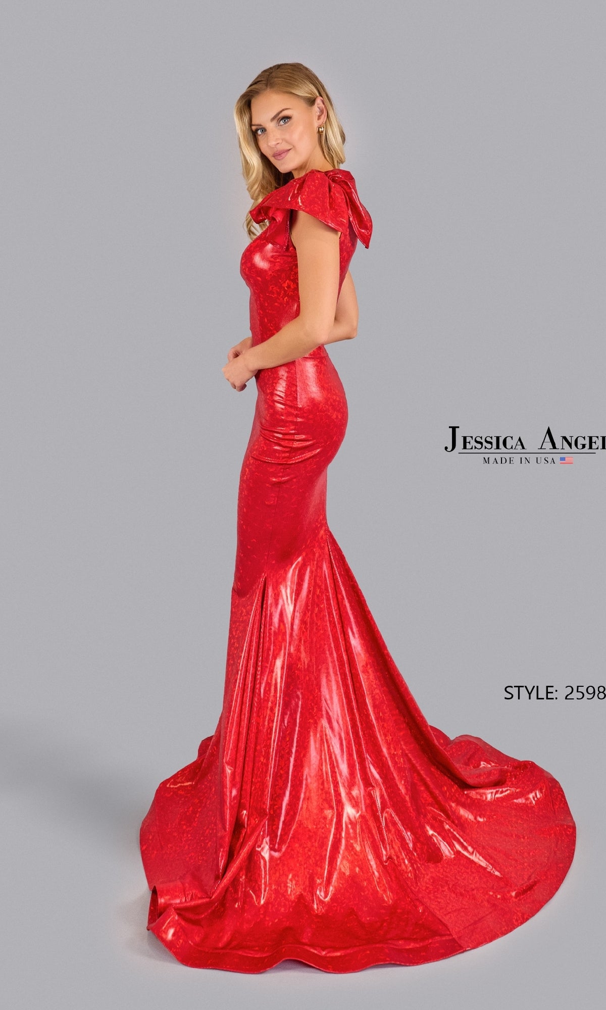 A woman poses against a plain gray background, wearing the Jessica Angel 2598 Mermaid Prom Dress with Bow—a fitted, floor-length, shiny red gown featuring a ruffled shoulder detail.